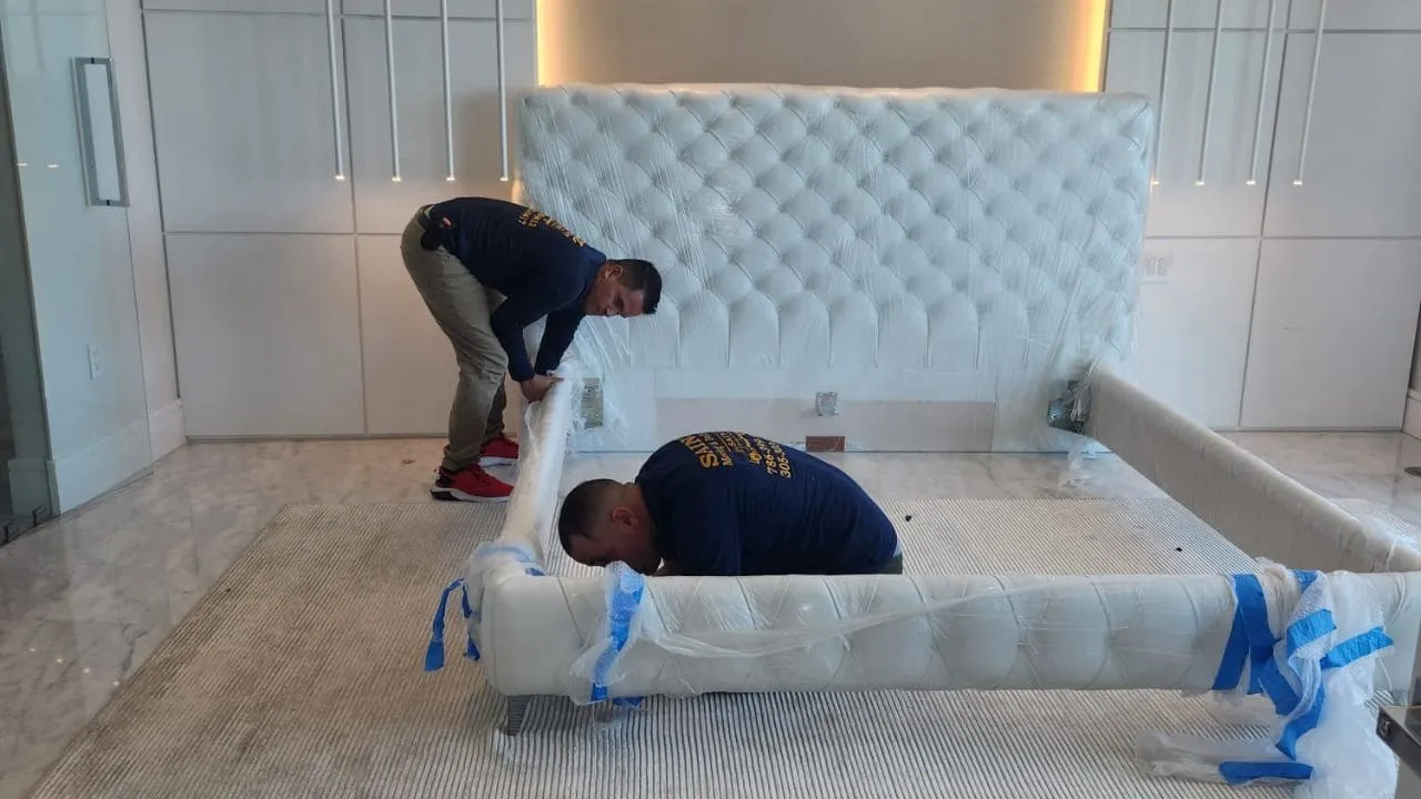 Sainz Moving crew members in company shirts wrapping and protecting a tufted bed frame